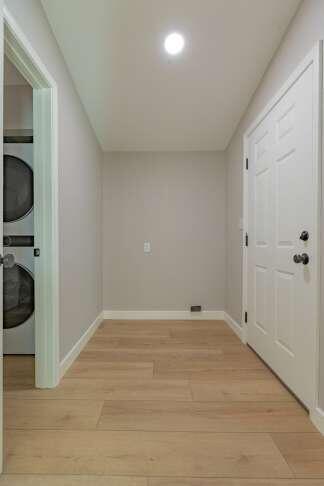 laundry area with stacked washer / drying machine and light hardwood / wood-style flooring