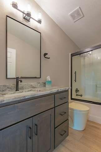 full bathroom featuring lofted ceiling, shower / bath combination with glass door, hardwood / wood-style flooring, vanity, and toilet