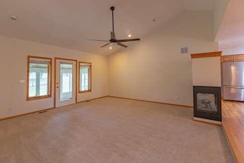 unfurnished living room featuring light colored carpet, visible vents, vaulted ceiling, and ceiling fan