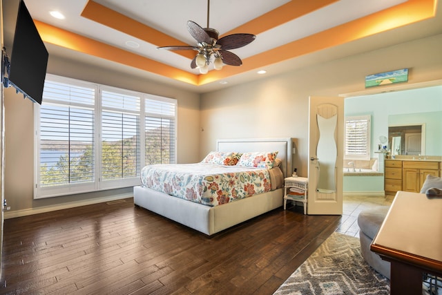 bedroom with ceiling fan, ensuite bathroom, dark hardwood / wood-style flooring, and a tray ceiling