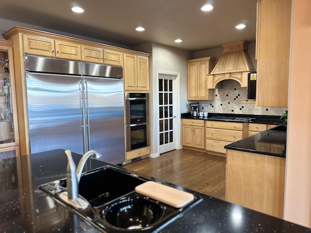 kitchen featuring light brown cabinetry, appliances with stainless steel finishes, decorative backsplash, wall chimney range hood, and dark hardwood / wood-style flooring