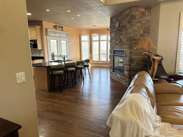 living room featuring sink, a stone fireplace, dark wood-type flooring, and a textured ceiling