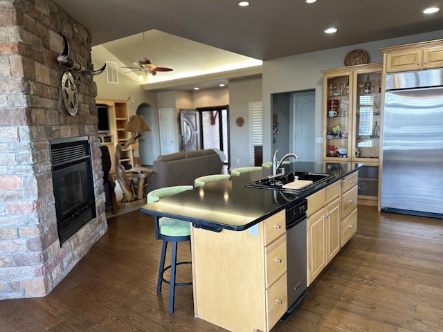 kitchen featuring a stone fireplace, stainless steel built in fridge, a kitchen breakfast bar, sink, and a center island with sink