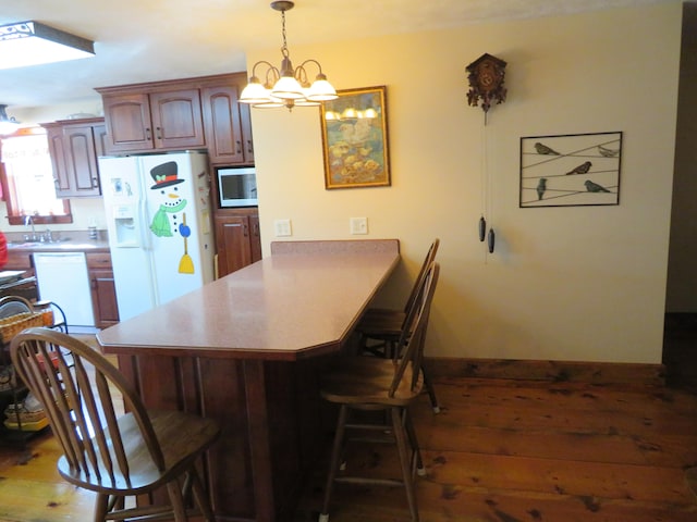 kitchen with dark hardwood / wood-style flooring, a breakfast bar area, white appliances, and kitchen peninsula