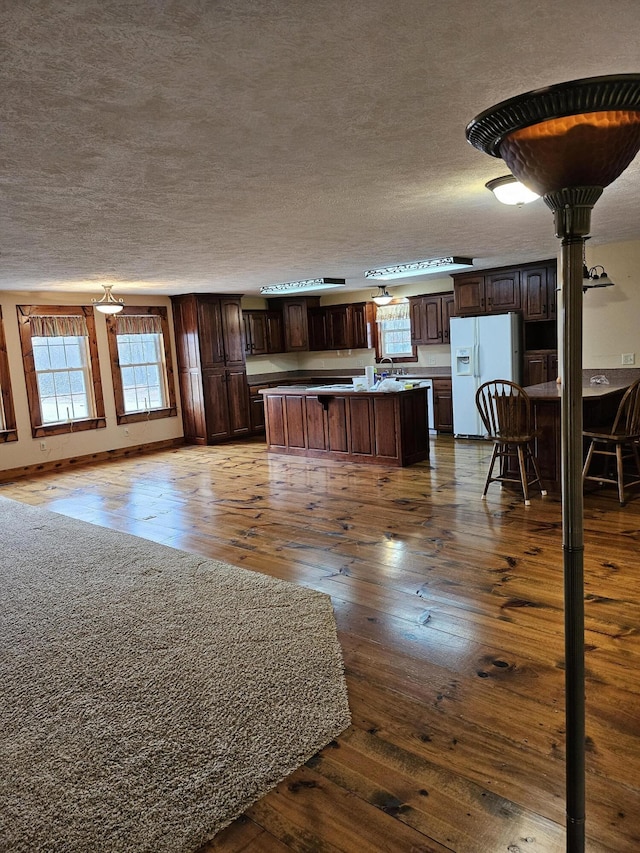 interior space featuring dark wood-type flooring, dark brown cabinets, a textured ceiling, a kitchen island, and white fridge with ice dispenser