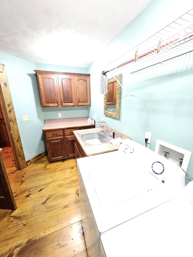 washroom featuring washer / clothes dryer, sink, light wood-type flooring, cabinets, and a textured ceiling