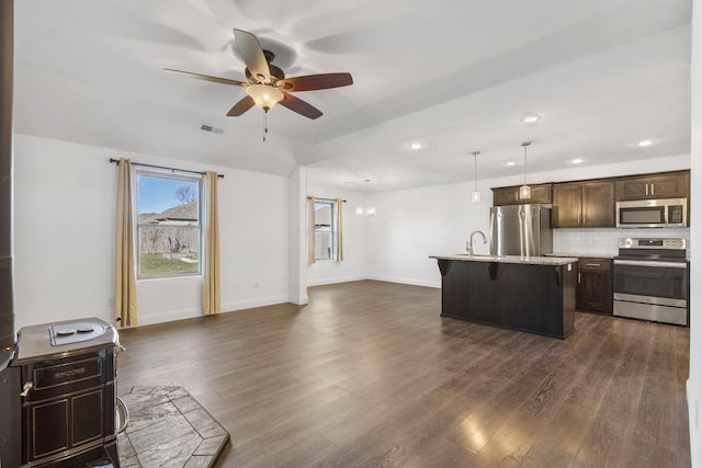 kitchen with pendant lighting, a kitchen breakfast bar, dark hardwood / wood-style floors, an island with sink, and stainless steel appliances