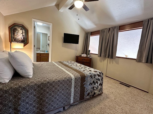 bedroom featuring carpet flooring, ceiling fan, vaulted ceiling with beams, ensuite bathroom, and a textured ceiling