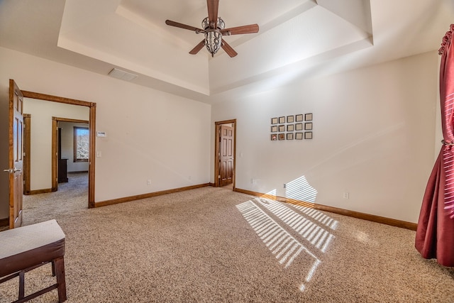 spare room with a raised ceiling, light carpet, and ceiling fan