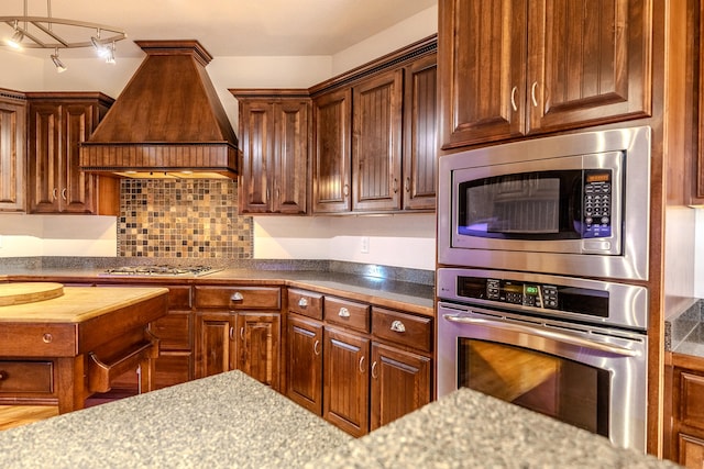 kitchen featuring butcher block countertops, decorative backsplash, custom exhaust hood, and appliances with stainless steel finishes