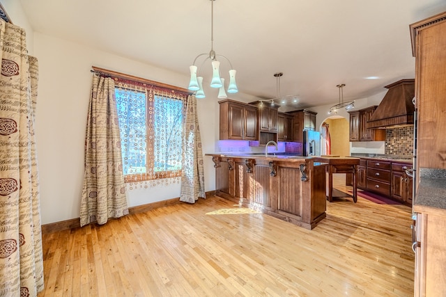 kitchen featuring stainless steel fridge with ice dispenser, decorative light fixtures, a breakfast bar area, custom range hood, and light wood-type flooring