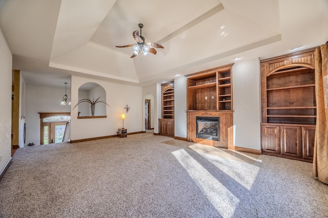 unfurnished living room featuring a raised ceiling, ceiling fan, built in features, and carpet flooring