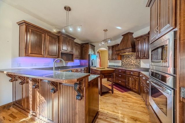 kitchen featuring a breakfast bar, premium range hood, light hardwood / wood-style flooring, appliances with stainless steel finishes, and kitchen peninsula