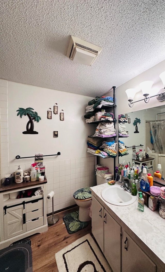 bathroom featuring a textured ceiling, toilet, vanity, tile walls, and hardwood / wood-style flooring