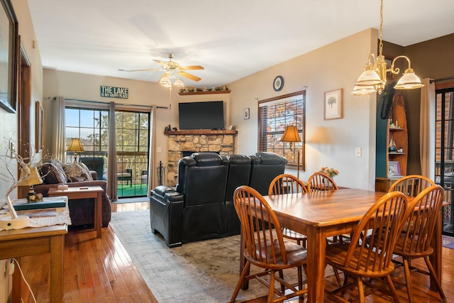 dining space with hardwood / wood-style floors, plenty of natural light, a stone fireplace, and ceiling fan with notable chandelier