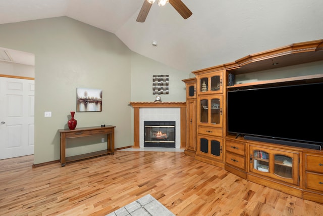 living room featuring a tile fireplace, light wood-type flooring, vaulted ceiling, and ceiling fan