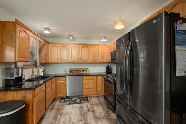 kitchen featuring appliances with stainless steel finishes, light hardwood / wood-style floors, dark stone countertops, and sink