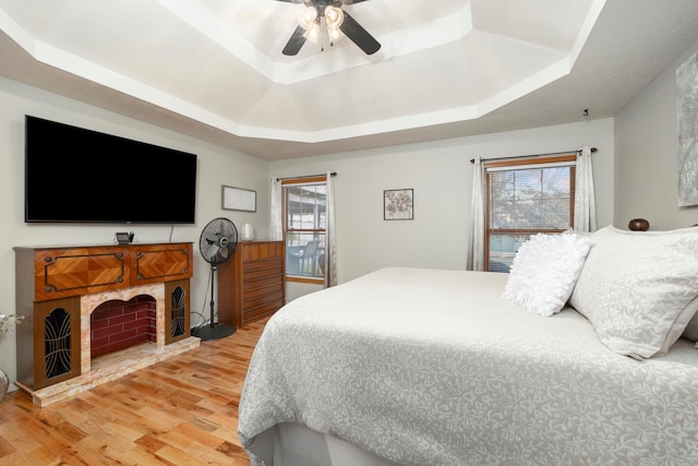 bedroom with ceiling fan, a raised ceiling, and light wood-type flooring