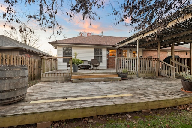 back house at dusk featuring a pergola and a wooden deck