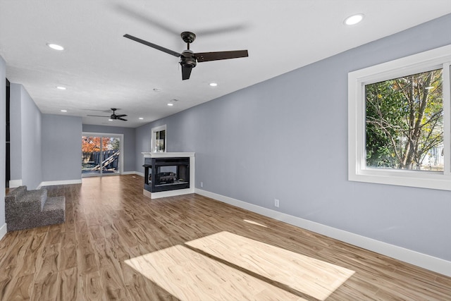 unfurnished living room with a multi sided fireplace, hardwood / wood-style floors, and ceiling fan