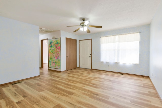 empty room with ceiling fan, light wood-type flooring, and a textured ceiling