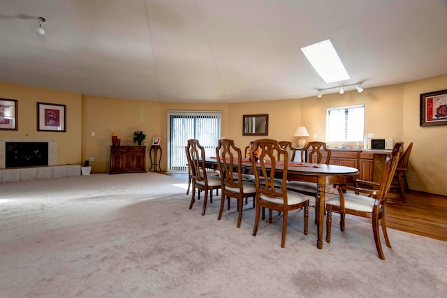 carpeted dining area with a skylight, a tile fireplace, and track lighting