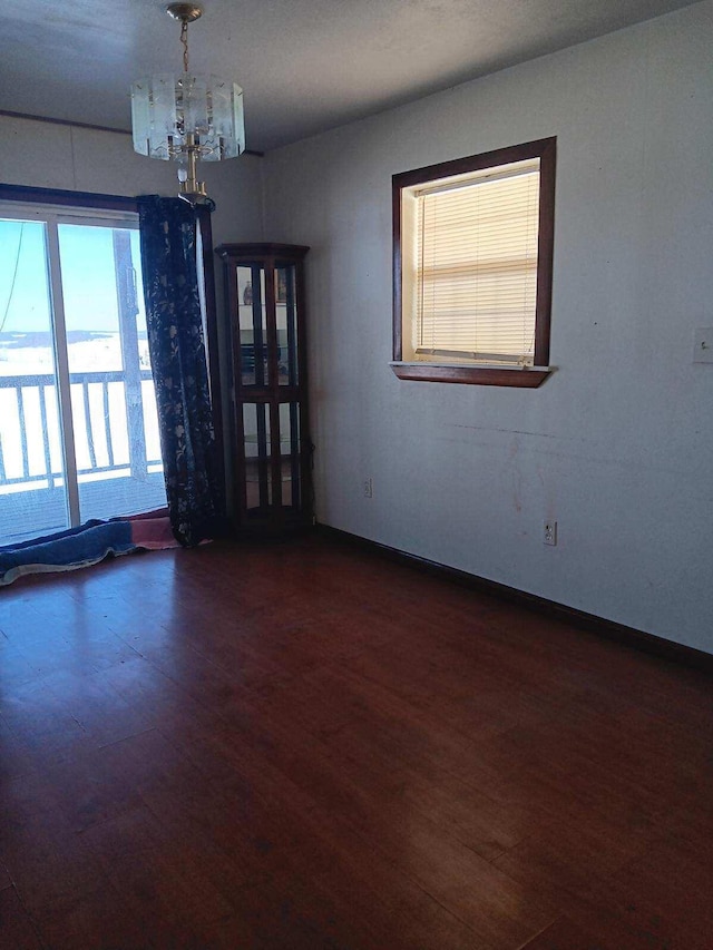 spare room featuring an inviting chandelier, baseboards, and wood finished floors