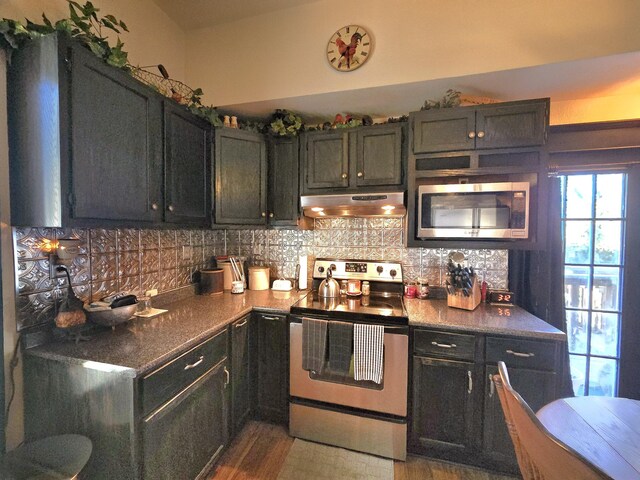 106 N Main St, Greenfield, MO 65661 - kitchen featuring stainless steel appliances, ventilation hood, decorative backsplash, wood finished floors, and dark countertops