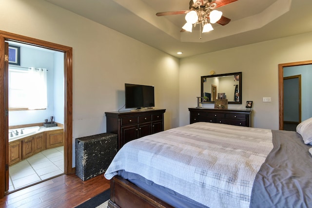 bedroom with a tray ceiling, ceiling fan, ensuite bathroom, and light hardwood / wood-style floors