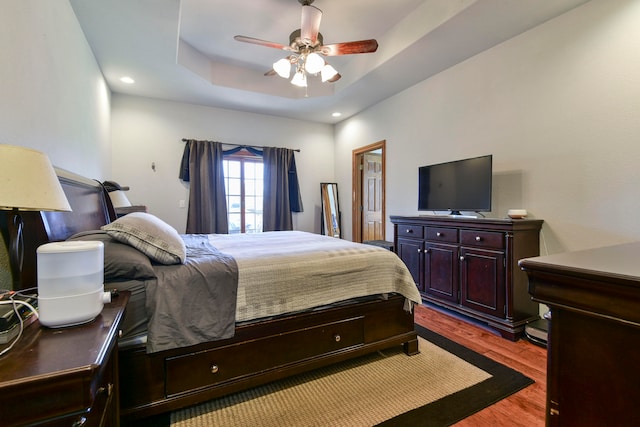 bedroom with ceiling fan, light hardwood / wood-style floors, and a tray ceiling