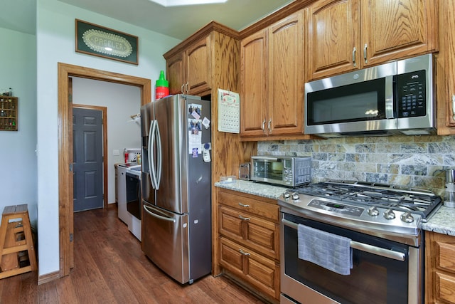 kitchen featuring dark wood-type flooring, stainless steel appliances, tasteful backsplash, separate washer and dryer, and light stone counters