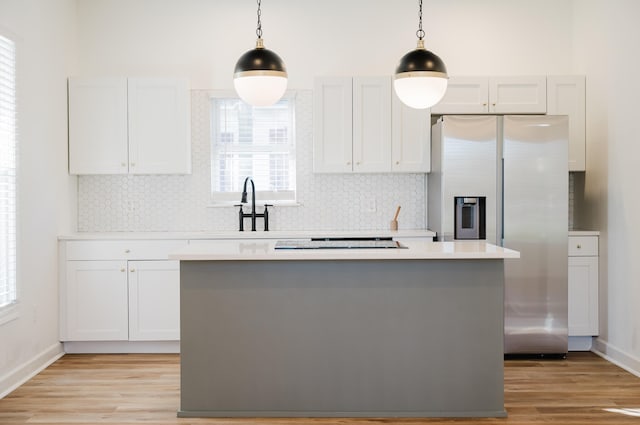 kitchen featuring stainless steel fridge, white cabinets, and hanging light fixtures