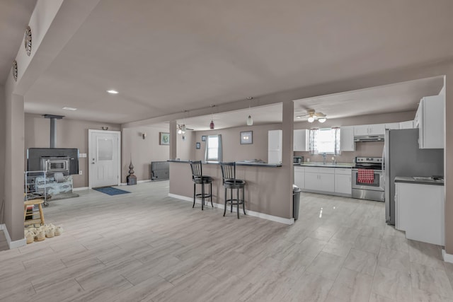 kitchen with a wood stove, ceiling fan, a kitchen bar, white cabinets, and appliances with stainless steel finishes