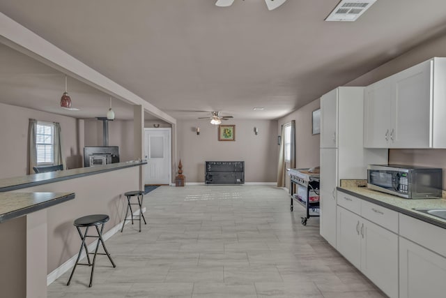 kitchen featuring appliances with stainless steel finishes, ceiling fan, pendant lighting, a wood stove, and white cabinetry