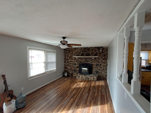 living room with a stone fireplace, ceiling fan, hardwood / wood-style floors, and a textured ceiling