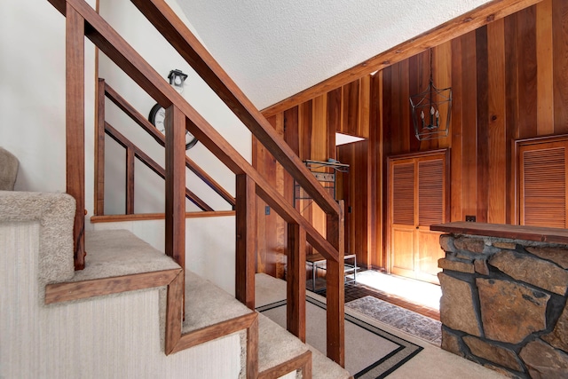 stairs with carpet flooring, a textured ceiling, and wooden walls