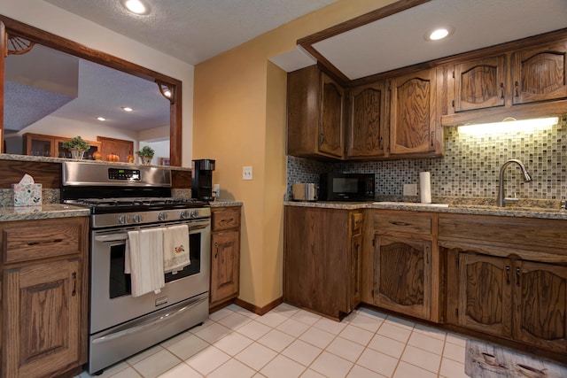 kitchen with stone counters, sink, tasteful backsplash, and stainless steel gas range