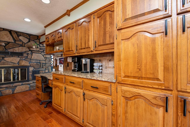 kitchen featuring light stone counters, dark hardwood / wood-style floors, crown molding, a textured ceiling, and a fireplace