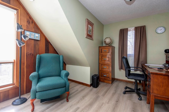 office with light hardwood / wood-style floors, a textured ceiling, wooden walls, and vaulted ceiling