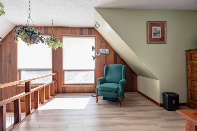 living area featuring wood walls, light hardwood / wood-style floors, lofted ceiling, and a textured ceiling