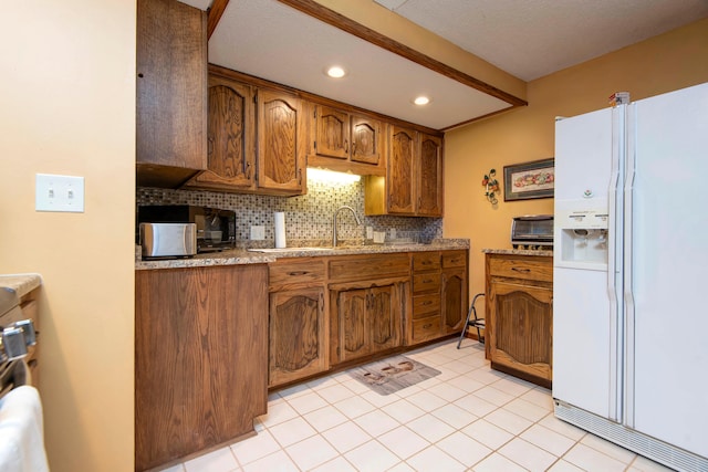 kitchen with decorative backsplash, light stone counters, white fridge with ice dispenser, and light tile patterned floors