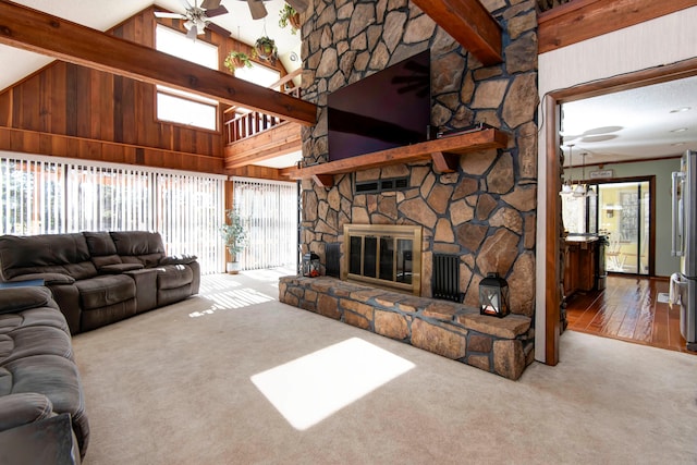 living room featuring beam ceiling, a stone fireplace, high vaulted ceiling, wooden walls, and hardwood / wood-style flooring