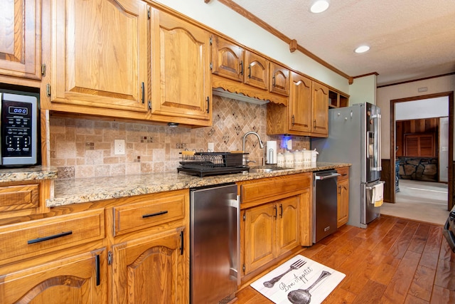 kitchen featuring light stone countertops, appliances with stainless steel finishes, a textured ceiling, crown molding, and light hardwood / wood-style flooring