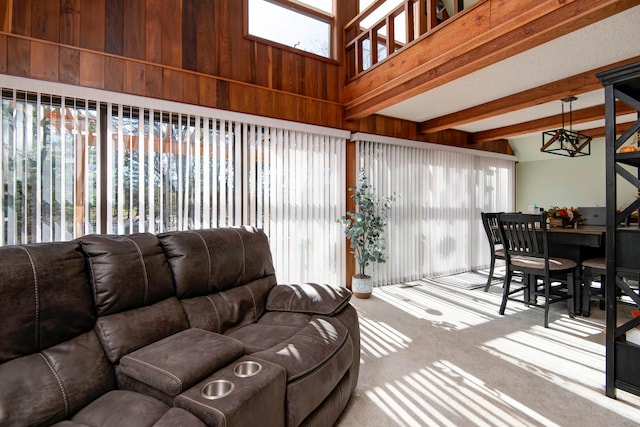 living room featuring beamed ceiling, high vaulted ceiling, a notable chandelier, wooden walls, and carpet