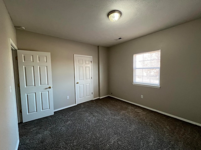 unfurnished bedroom with dark colored carpet, a textured ceiling, and a closet