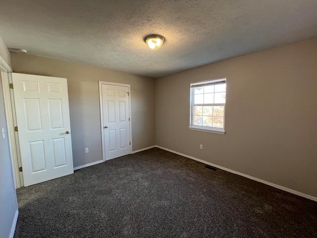 unfurnished bedroom featuring a closet, a textured ceiling, and dark colored carpet