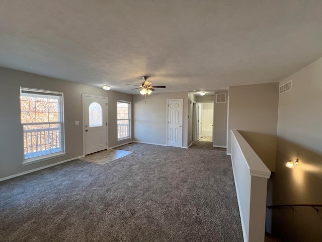 unfurnished living room with dark colored carpet, a textured ceiling, ceiling fan, and a healthy amount of sunlight