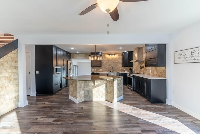 kitchen with wall chimney exhaust hood, hanging light fixtures, dark wood-type flooring, stainless steel appliances, and backsplash