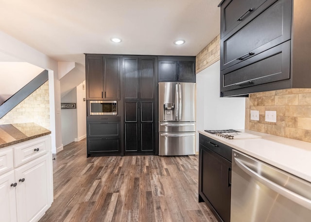 kitchen featuring decorative backsplash, stainless steel appliances, light stone countertops, and dark wood-type flooring