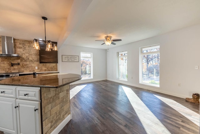 kitchen with dark wood-type flooring, dark stone counters, white cabinets, wall chimney range hood, and tasteful backsplash